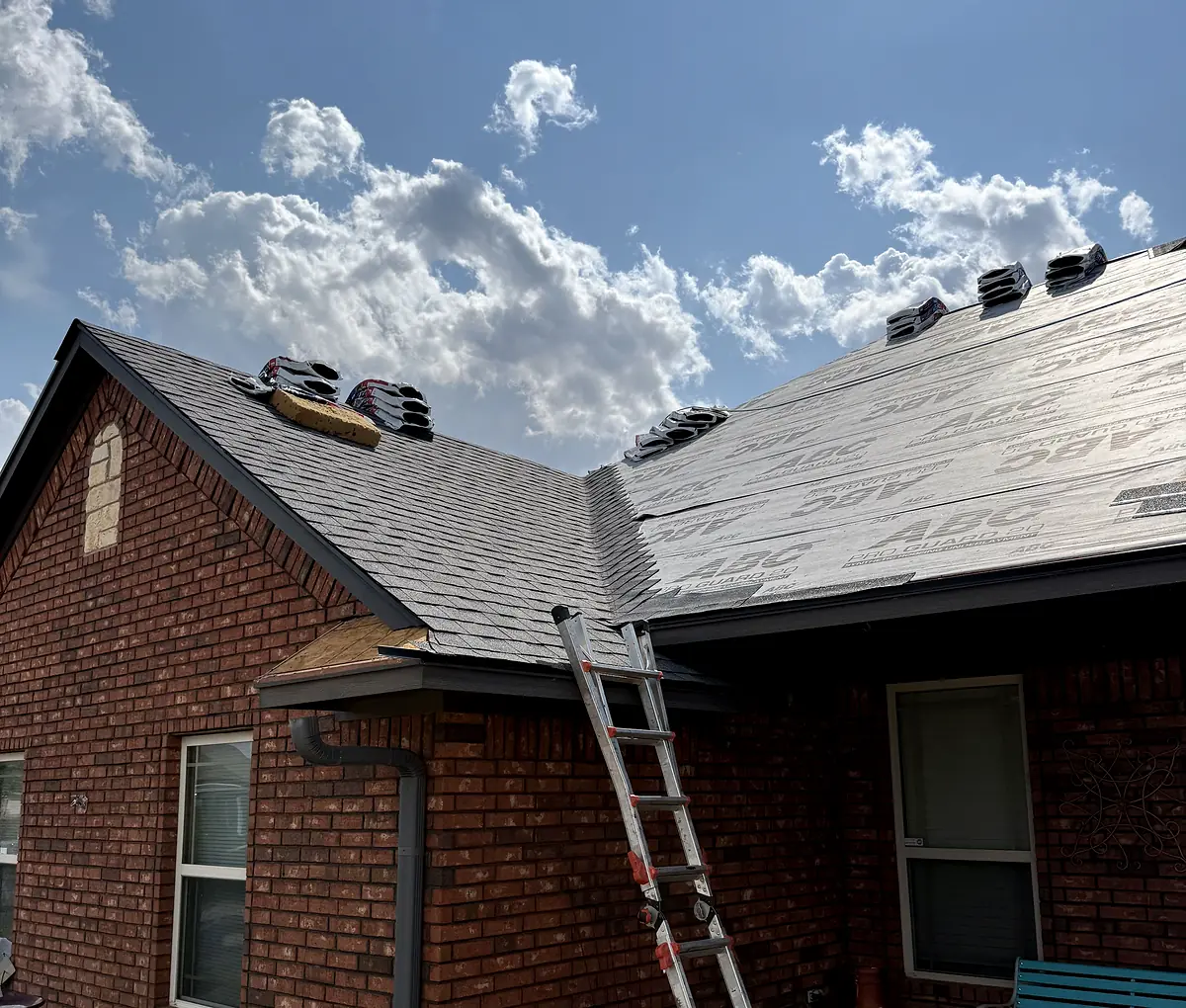 Roofing work in progress on a brick home, with shingles on part of the roof and underlayment on the rest